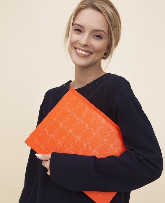 smiling woman standing while holding orange folder