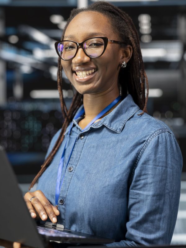 Portrait of smiling technician in data center monitoring system performance with laptop, identifying bottlenecks. Happy server hub employee troubleshooting errors, implementing optimizations