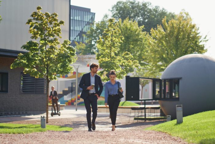 Smiling managers strolling downtown in sunny morning. Business couple in suits talking holding coffee. Joyful corporate people commuting going city park. Relaxed man woman discussing company project